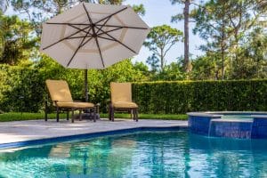 Outdoor swimming pool with a raised spa, lounge chairs, and a large patio umbrella surrounded by lush landscaping and trees.